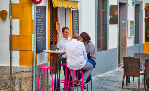 A couple talking to a waiter whilst sitting at a table outside a bar in Spain