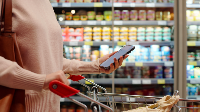 A woman pushing a shopping trolley and holding a mobile phone
