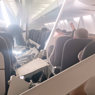 Airplane cabin interior with collapsed white plastic ceiling panels resting on seats and passengers.
