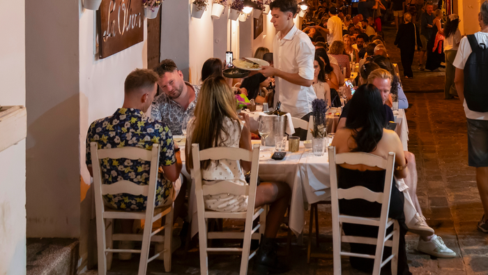 Diners eating outdoors at a restaurant next to a busy street