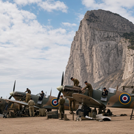Colorized WWII photo of RAF Spitfires being serviced on the airfield at Gibraltar, with the Rock of Gibraltar in the background.