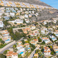 Aerial view of a hillside urbanización of white and terracotta-roofed villas with private pools in Spain.