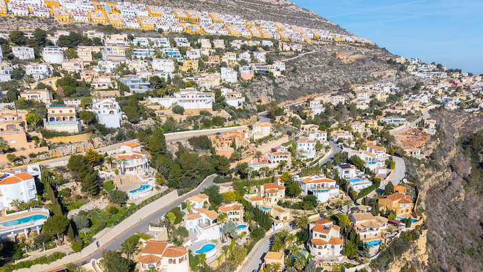 Aerial view of a hillside urbanización of white and terracotta-roofed villas with private pools in Spain.