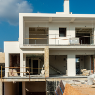 A part-built two-storey house on a Spanish housing development, with an excavated foundation pit and building materials in the foreground.