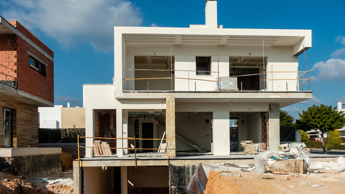 A part-built two-storey house on a Spanish housing development, with an excavated foundation pit and building materials in the foreground.