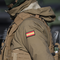 A Spanish soldier wearing tactical gear and a small Spanish flag patch on their left arm.