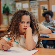 Girl sits at her desk with a bored expression on her face in a primary school classroom looking forward.