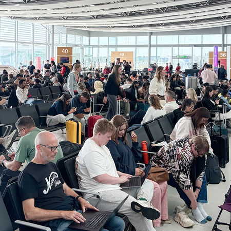 Passengers wait with luggage in a crowded airport departure lounge.
