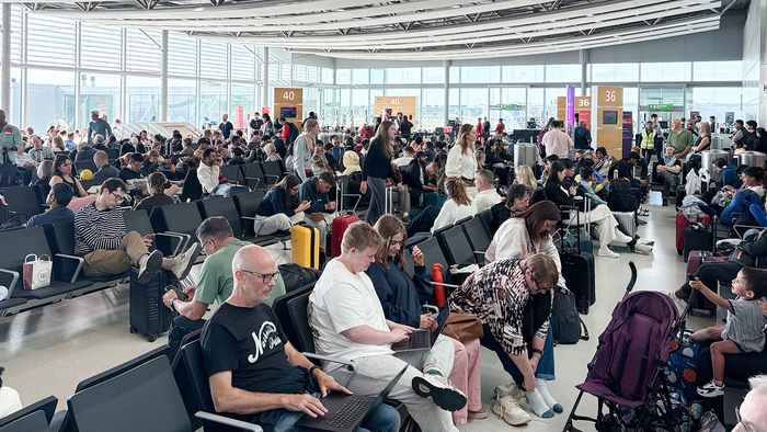 Passengers wait with luggage in a crowded airport departure lounge.