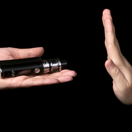 A hand offers a black vape device while another hand held up in a stop gesture refuses it, against a plain black background.