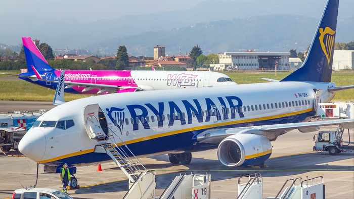 A Ryanair Boeing 737 parked at an airport gate with a Wizz Air Airbus taxiing behind it.
