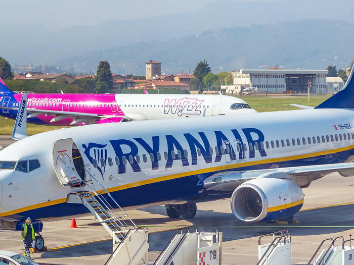 A Ryanair Boeing 737 parked at an airport gate with a Wizz Air Airbus taxiing behind it.
