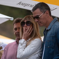 Begoña Gómez stands beside Pedro Sánchez at an outdoor public event in Spain.