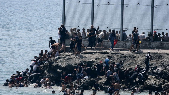 Large group of migrants climb rocks and enter Ceuta from Morocco beside the border fence during the July 2026 invasion.