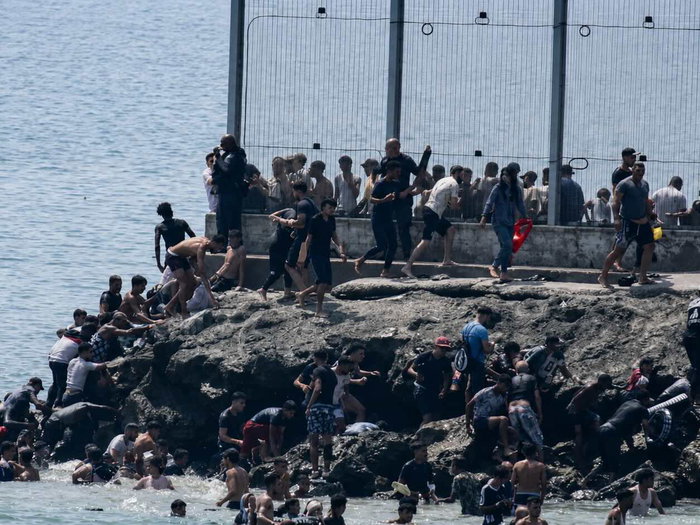 Large group of migrants climb rocks and enter Ceuta from Morocco beside the border fence during the July 2026 invasion.