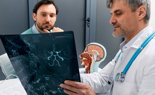 A male doctor holding and reviewing a magnetic resonance imaging (MRI) brain scan film with a attentive male patient in a clinic.