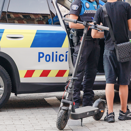 Local Police officers speak with a teenager standing beside an electric scooter next to a patrol car on a Spanish city street.