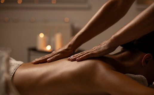 Relaxed young woman lying face down enjoying professional back massage in serene spa setting with candles, side view