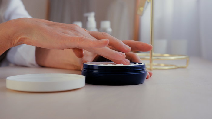 Woman's hand applying wrinkle cream from a pot