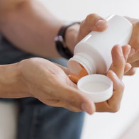 a man sitting down and emptying some pills into his hands from a pot