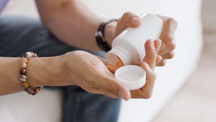 a man sitting down and emptying some pills into his hands from a pot