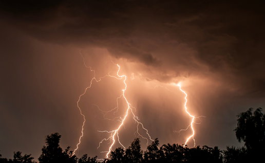 Lightning bolts fall on a forest at night