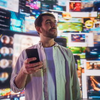 Portrait of Caucasian Man Using Smartphone in Metaverse With Animated Stream Of Interfaces With Social Media, e-Commerce Shopping, Internet Influencers And Games. Visualization Of Web Network.