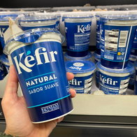 A hand holding a Kefir yogurt with others in the refrigerator in the background