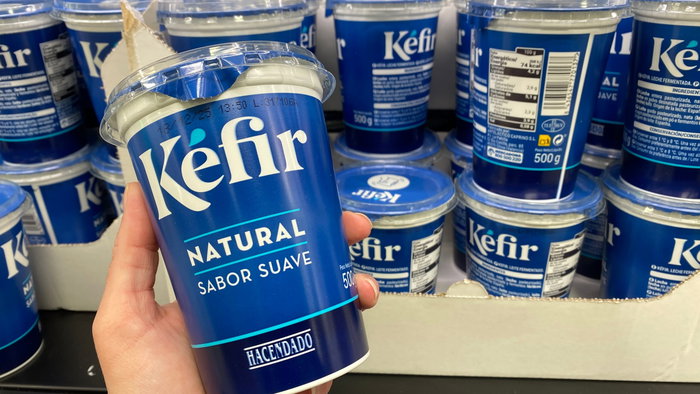 A hand holding a Kefir yogurt with others in the refrigerator in the background