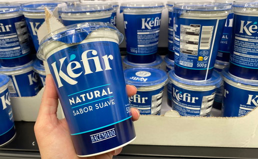 A hand holding a Kefir yogurt with others in the refrigerator in the background