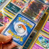 A mans hand holding Pokémon trading cards in an Album