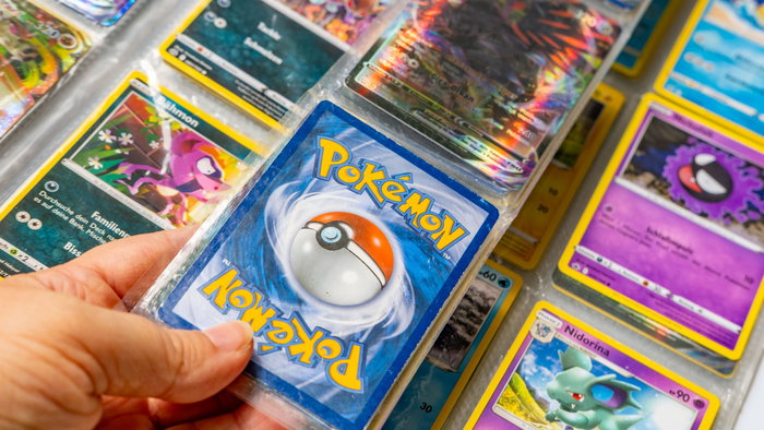 A mans hand holding Pokémon trading cards in an Album
