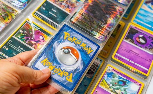 A mans hand holding Pokémon trading cards in an Album
