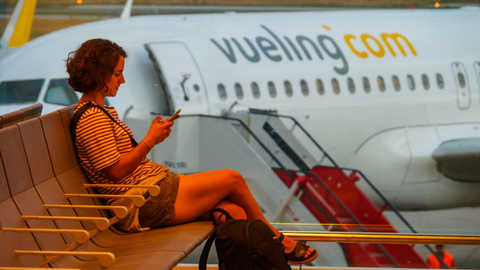 Woman siting in an airport with a Vueling aircraft in the background