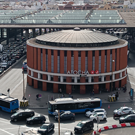 Aerial view of Madrid’s Atocha railway station, with its round red-brick entrance building and glass roof, surrounded by queuing taxis, buses and traffic.