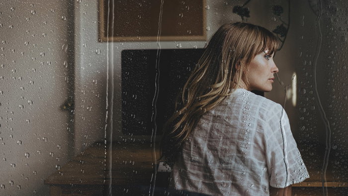 Woman looking through a rain-covered window as Airbnb introduces new holiday rain insurance