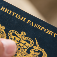 A hand holding a dark blue British passport, with gold lettering and the royal coat of arms on the cover