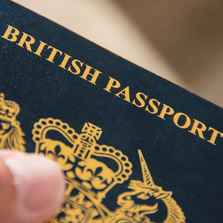 A hand holding a dark blue British passport, with gold lettering and the royal coat of arms on the cover