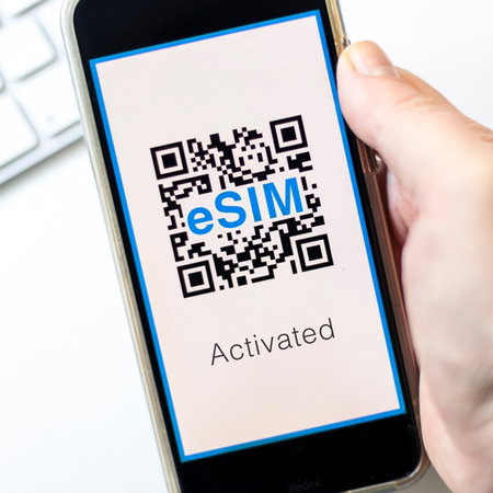 Hand holding a mobile phone with a QR code on the screen for eSim saying activated