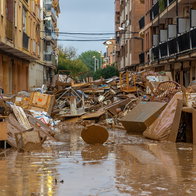Flood-damaged residential street covered in mud, debris and destroyed furniture following severe flooding.