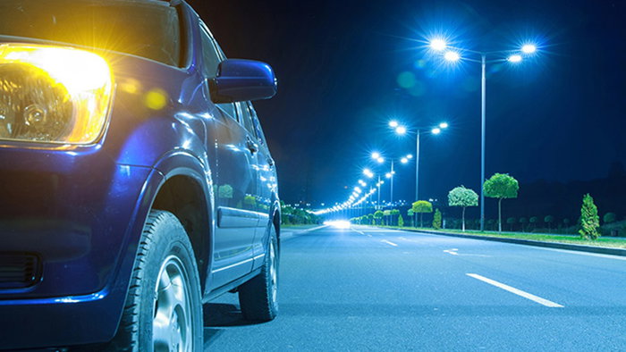 Car with headlights on beside a brightly lit road at night.