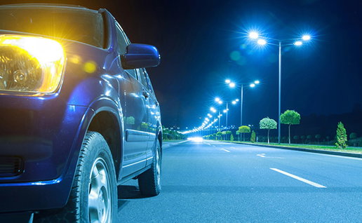 Car with headlights on beside a brightly lit road at night.
