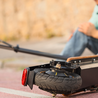 A man in a white helmet sits on a red cycle lane holding his knee, with a fallen electric scooter lying in the foreground.