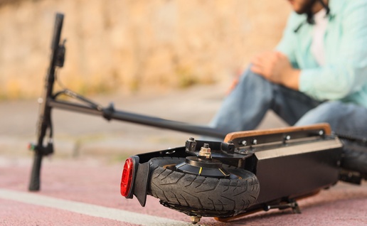 A man in a white helmet sits on a red cycle lane holding his knee, with a fallen electric scooter lying in the foreground.