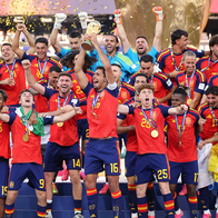Spain’s football team celebrating on a podium in red shirts and winners’ medals as the captain lifts the World Cup trophy and gold confetti falls.