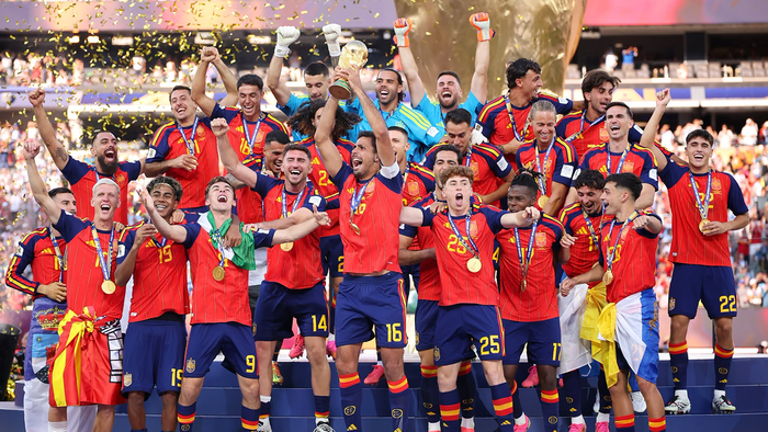 Spain’s football team celebrating on a podium in red shirts and winners’ medals as the captain lifts the World Cup trophy and gold confetti falls.