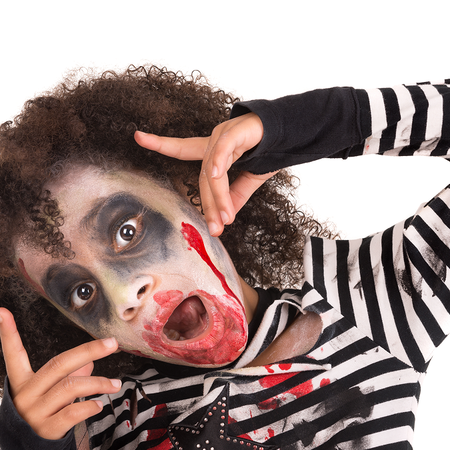 Child with curly hair in zombie makeup, with dark eye shadow and fake blood around the mouth, wearing a black and white striped top and posing against a white background.