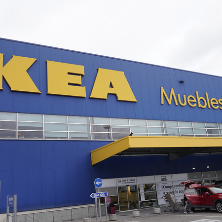 The front of an IKEA store with a blue wall, the yellow IKEA logo and the words “Muebles y decoración”, and cars parked by the entrance under a yellow canopy.