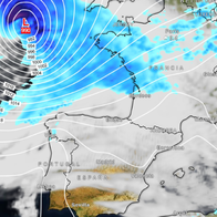 Weather map of western Europe showing a deep low-pressure system marked L 990 to the north-west of France, ringed by curved white pressure lines, with blue bands of rain over the sea, the English Channel and France, and mostly cloudy but dry skies over Spain and Portugal.