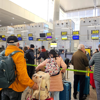 Travellers with backpacks and suitcases queue at a row of numbered check-in desks in an airport terminal.